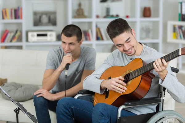Άνθρωπο σε αναπηρικό καροτσάκι να παίζει κιθάρα, φίλος τραγουδώντας στο μικρόφωνο — Φωτογραφία Αρχείου