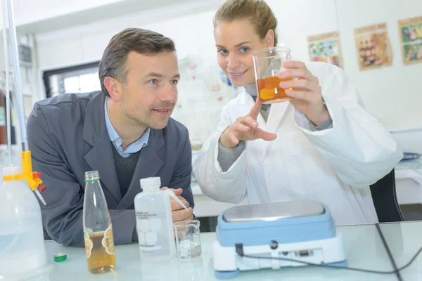 Técnico de laboratorio mezclando líquidos en el laboratorio mientras asistente escribir datos — Foto de Stock