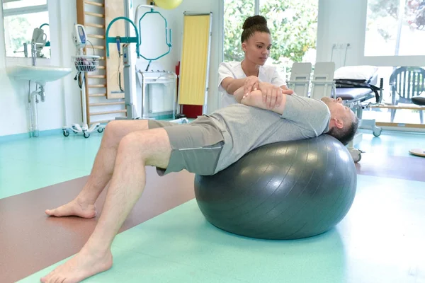 Hombre con fisioterapeuta inclinado hacia atrás en la bola aeróbica —  Fotos de Stock