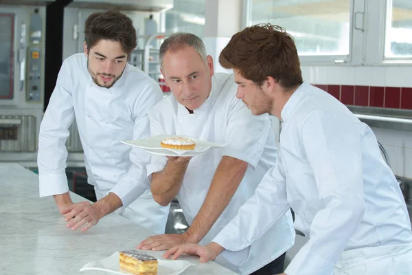 Seniorchef zeigt Auszubildenden Kuchen — Stockfoto