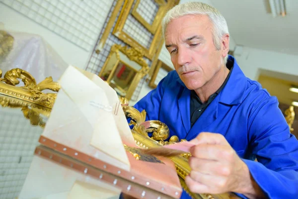 Homem aplicando folha de ouro a um espelho — Fotografia de Stock