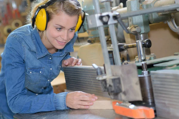 Jonge vrouwelijke timmerman in veiligheid apparatuur snijden hout in werkplaats — Stockfoto