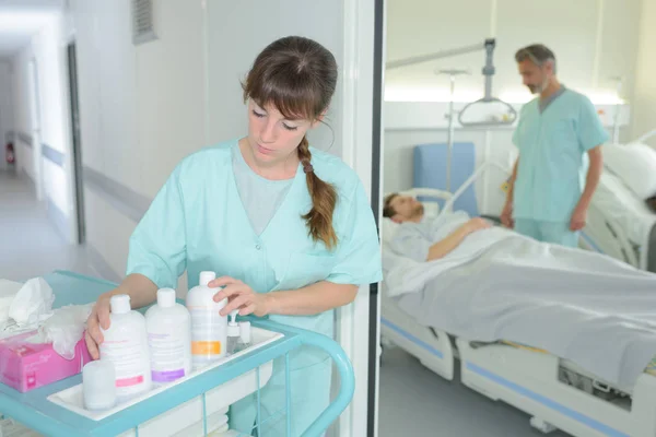 Enfermeira com carrinho no corredor, enquanto o médico assistente paciente — Fotografia de Stock