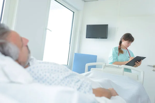 Läkare tar anteckningar från man patienten liggande i sjukhussäng — Stockfoto