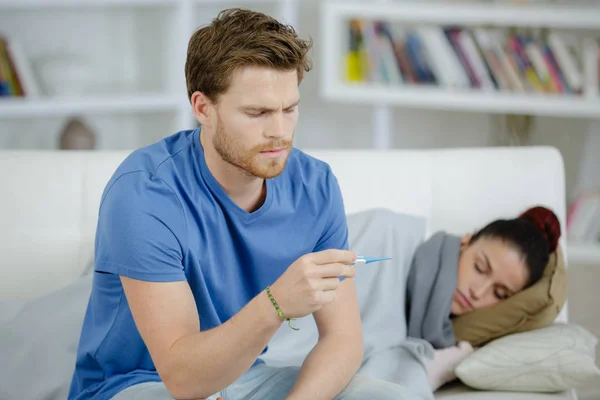 Mulher doente com namorado monitorando sua temperatura com termômetro — Fotografia de Stock