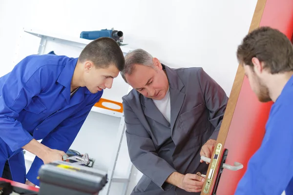 Charpentier mâle et apprentis fixant serrure de porte — Photo