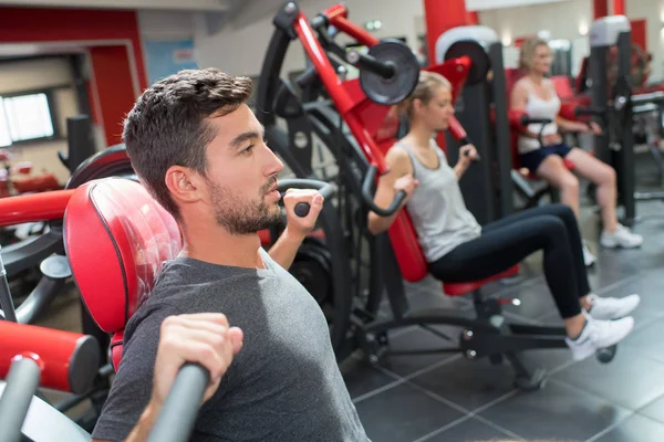 Deportistas ejercitando los músculos en la máquina de levantamiento de pesas gimnasio —  Fotos de Stock