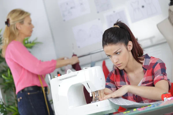 Женщина регулирует швейную машинку при изготовлении одежды — стоковое фото