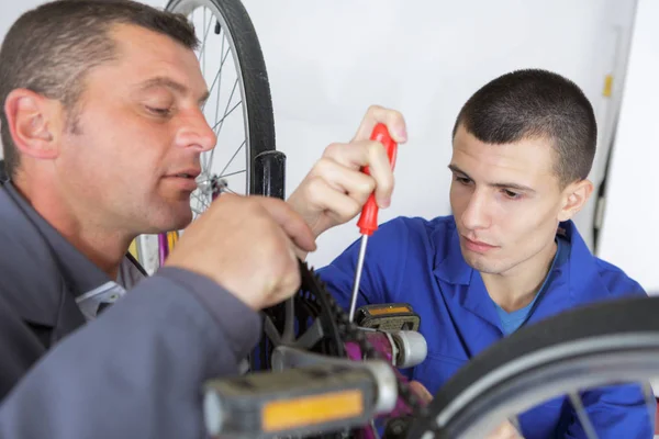 Fiets monteur en leerling reparatie van een fiets in de werkplaats — Stockfoto