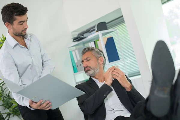 Assistent zeigt dem Manager, der seine Füße auf dem Schreibtisch hat, die Datei — Stockfoto