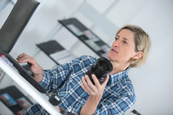 コンピューターとオフィスでカメラを持つ女性カメラマン — ストック写真