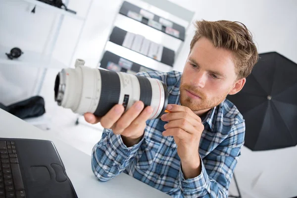 Joven fotógrafo limpiando lentes en su estudio —  Fotos de Stock