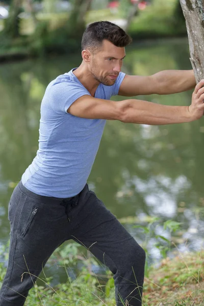 Rear view of man standing by lake and stretching arms — Stock Photo, Image