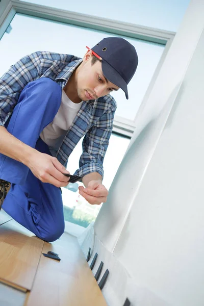 Giovane lavoratore in uniforme installazione nuovo battiscopa a casa — Foto Stock