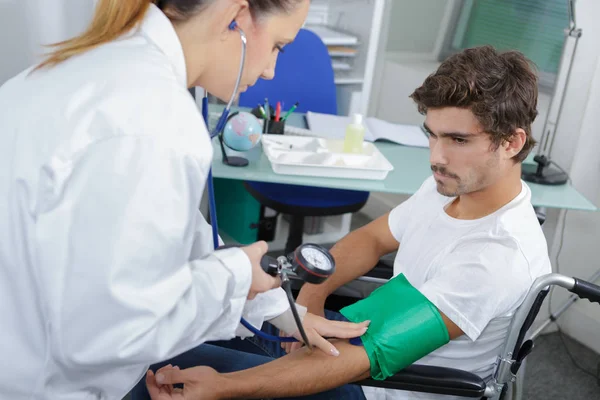 Lekarka sprawdzanie pacjenta ciśnienia krwi na wózkach — Zdjęcie stockowe