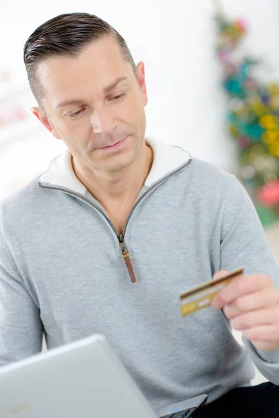 Człowiek w laptopie trzyma karty kredytowej, choinki w tle — Zdjęcie stockowe