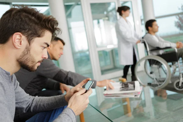 Homme utiliser un téléphone intelligent tout en attendant dans une clinique — Photo