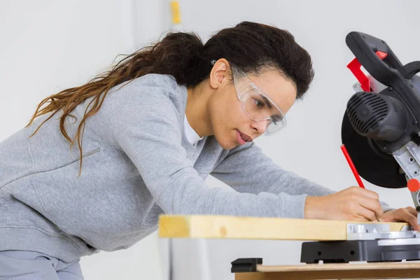 Woman marking where to cut wood with circular saw — Stock Photo, Image