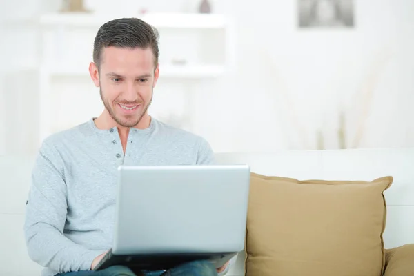 Młody człowiek z laptopem na kanapie w pokoju — Zdjęcie stockowe