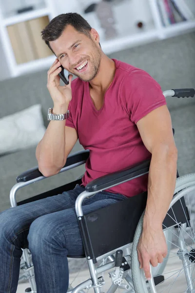 Un hombre guapo en silla de ruedas hablando por teléfono y sonriendo —  Fotos de Stock