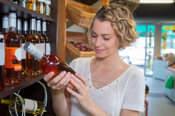 Jovem mulher escolhendo vinho rosa em uma loja de bebidas — Fotografia de Stock