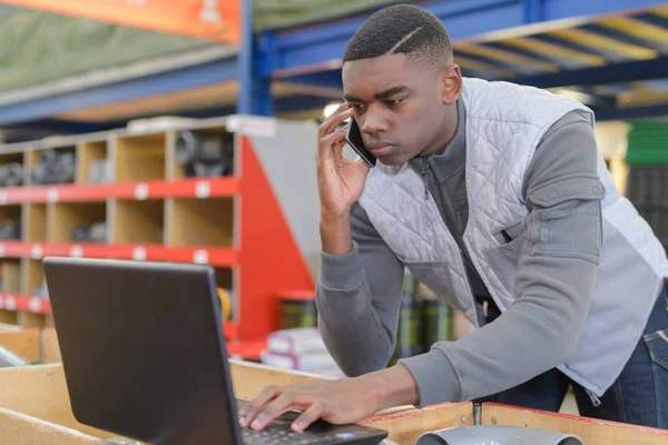 Gerente de armazém usando telefone e laptop em um grande armazém — Fotografia de Stock