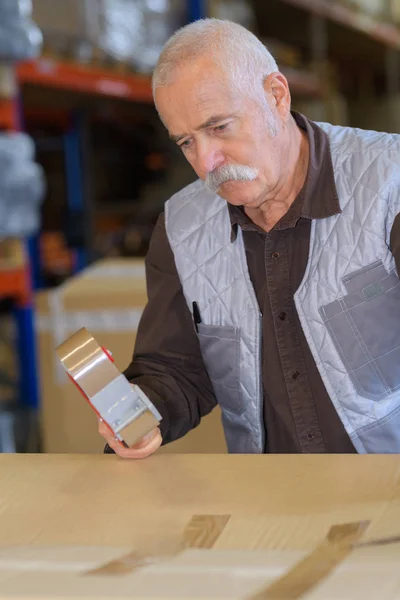 Senior man afdichten kartonnen doos met een tape dispenser — Stockfoto