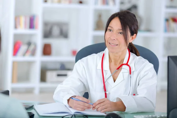 Hermosa joven sonriente doctora sentada en el escritorio — Foto de Stock