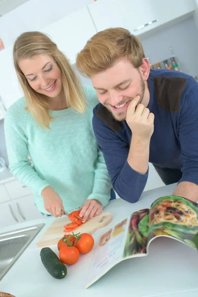 Пара обнимается на кухне, проверяя книгу рецептов — стоковое фото