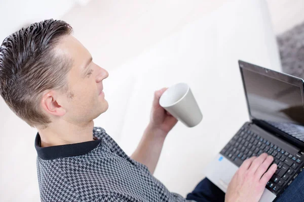 Joven sosteniendo la taza de café con el ordenador portátil en el escritorio — Foto de Stock