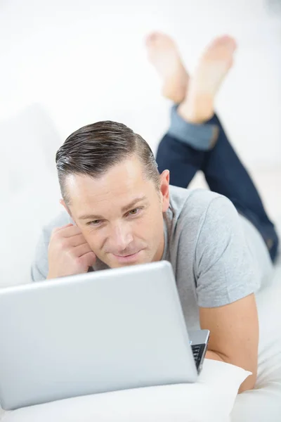 Pensive guy lying on bed with laptop — Stock Photo, Image