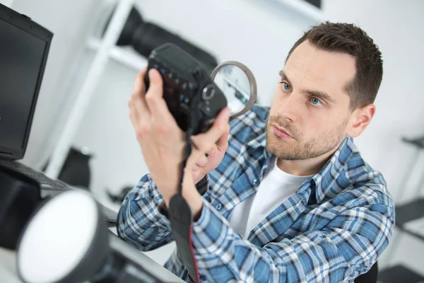 Man looking at camera body with magnifying glass — Stock Photo, Image