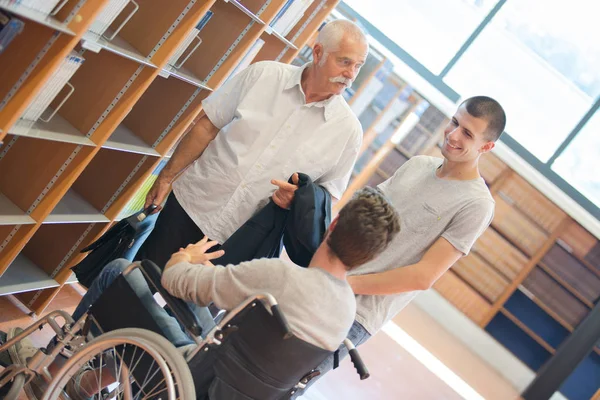 Studente in sedia a rotelle che parla con compagno di classe e professore in biblioteca — Foto Stock