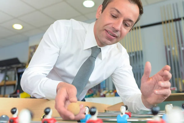 Man wearing shirt and tie replacing ball onto table football game — Stock Photo, Image