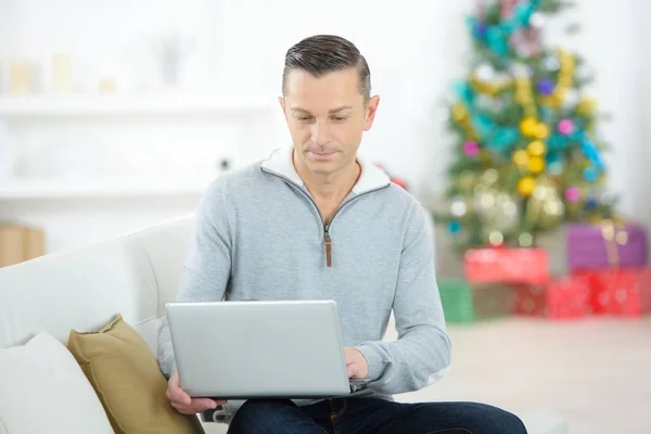 Człowiek z laptopem na kanapie w okresie Bożego Narodzenia — Zdjęcie stockowe
