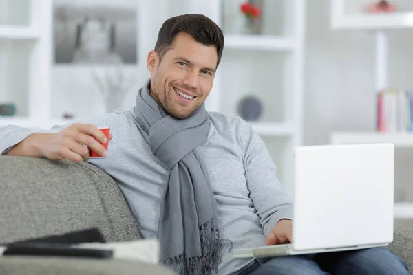 Hombre joven sonriendo mientras usa el ordenador portátil en la sala de estar — Foto de Stock
