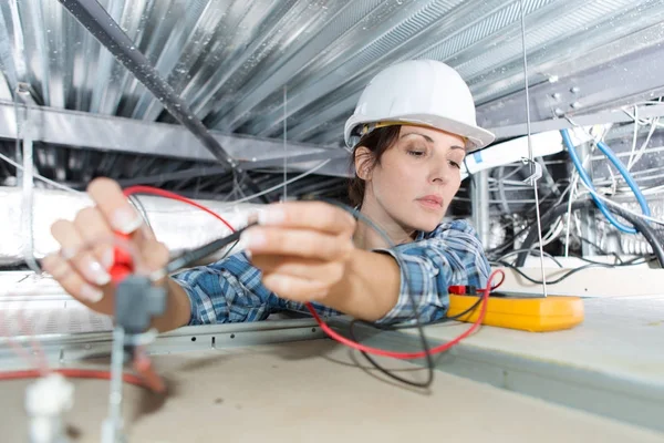 Electricista hembra comprobando voltaje de cables de techo —  Fotos de Stock