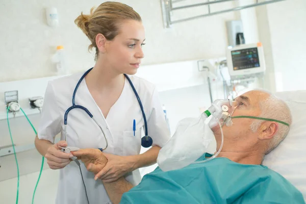 Médico feminino auxiliando o homem idoso usando máscara de oxigênio na clínica — Fotografia de Stock