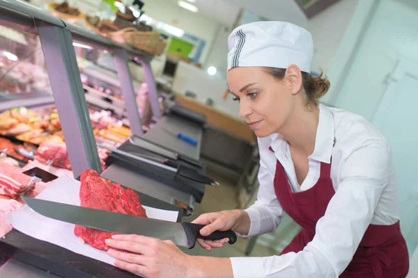Una carnicera cortando una carne — Foto de Stock