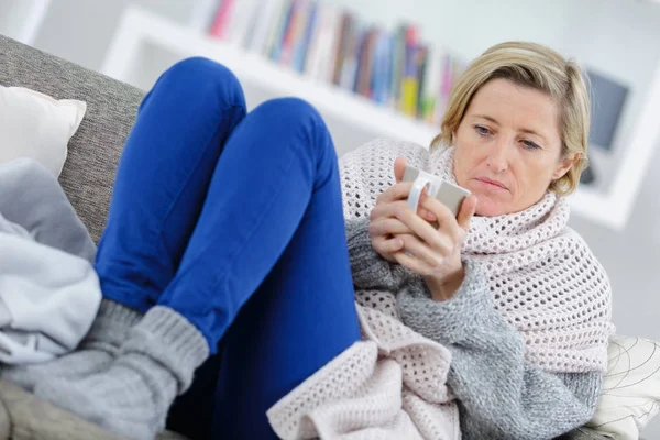 Blond sjuk kvinna handpåläggning i soffan med mugg — Stockfoto