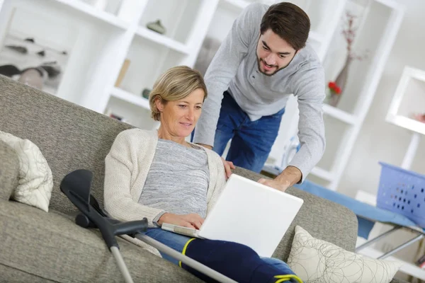 Medelålders kvinna skadade sitter på soffan och använder bärbar dator — Stockfoto