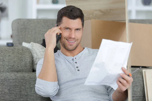Χαμογελαστός άνθρωπος χρησιμοποιεί κινητό τηλέφωνο κοντά σε χαρτί στο σπίτι — Φωτογραφία Αρχείου