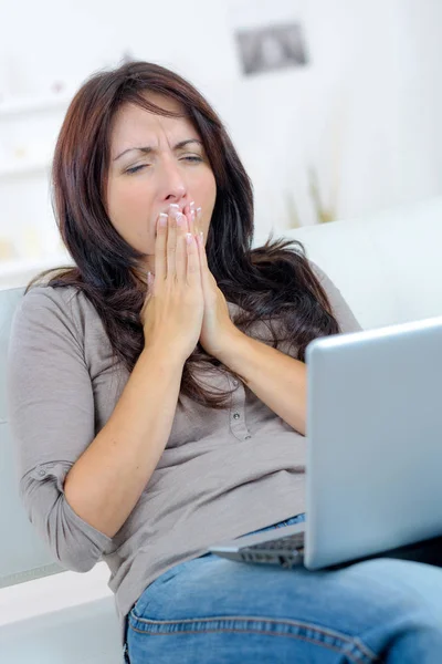 Trött kvinna gäspar med laptop i soffan hemma — Stockfoto