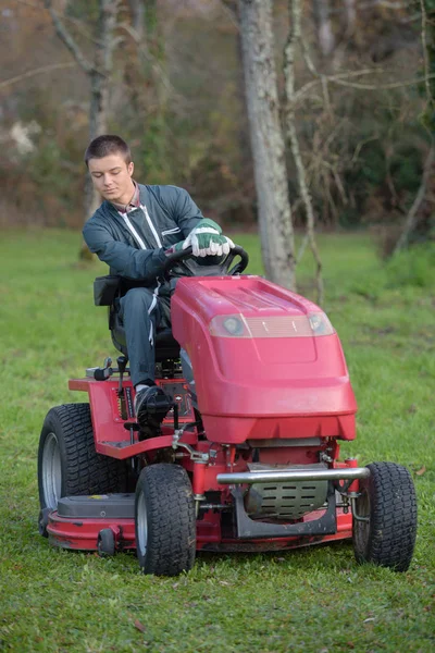 Junger Mann fährt Rasenmäher — Stockfoto