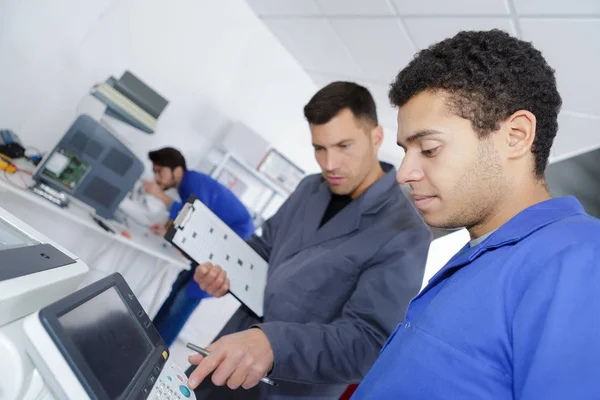 Aprendiz masculino trabajando con ingeniero en maquinaria CNC —  Fotos de Stock