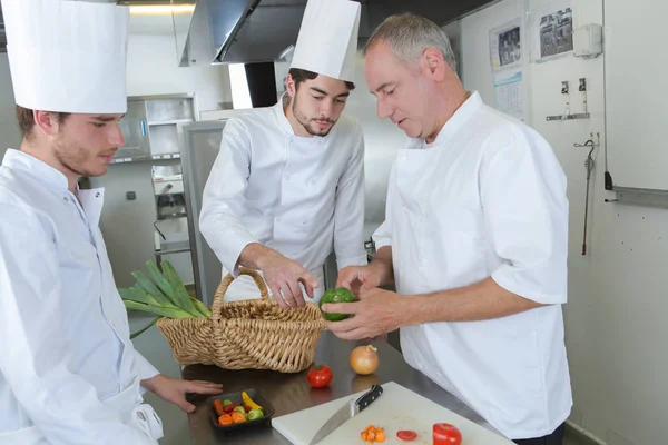 Chef cuisinier enseignant à ses collègues comment trancher des légumes — Photo