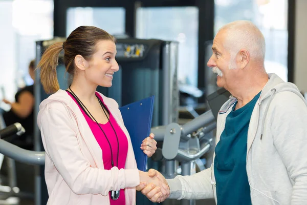 Kvinnliga tränare mötesklienten senior mannen på gym club — Stockfoto