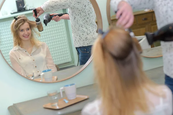 Cabeleireiro cuidadosamente escovando cabelo clientes em reflexão no espelho — Fotografia de Stock