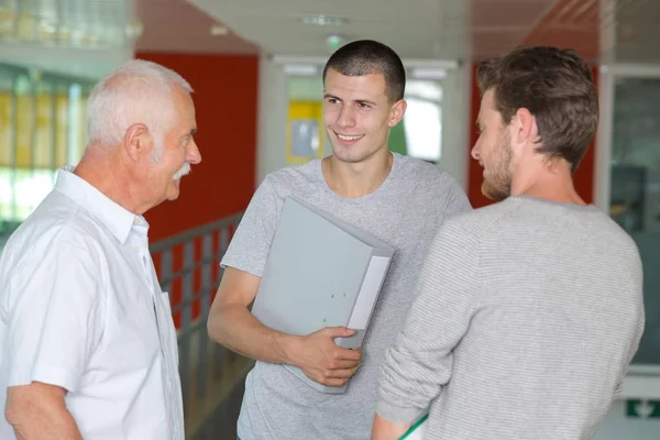 Професор з ноутбуком, що розмовляє з двома студентами в коридорі — стокове фото