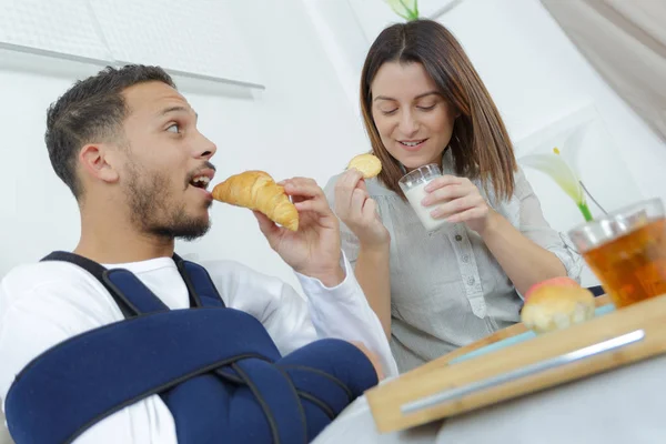 Young couple eating croissants on breakfast in bed — Stock Photo, Image